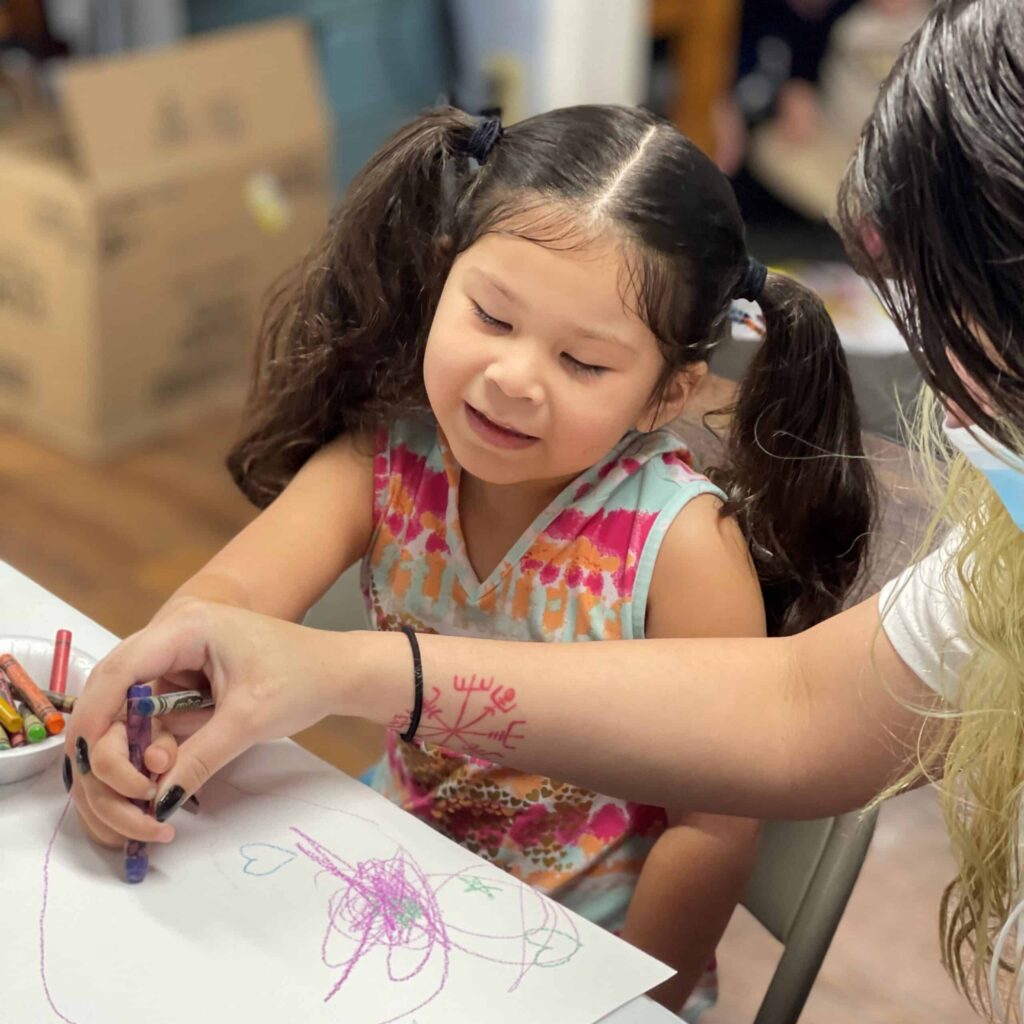 A young girl and her mother color on a piece of paper