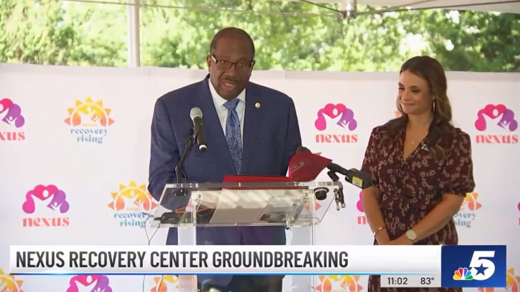 Man and woman at a podium in front of a Nexus Recovery Rising banner