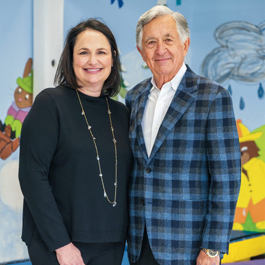 Two people posing for a photo in front of a large child's drawing