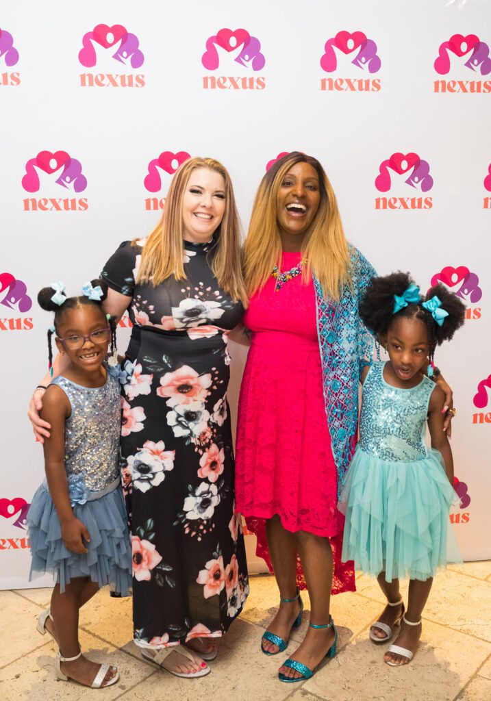 Women and children smiling for a photo in front of a Nexus backdrop